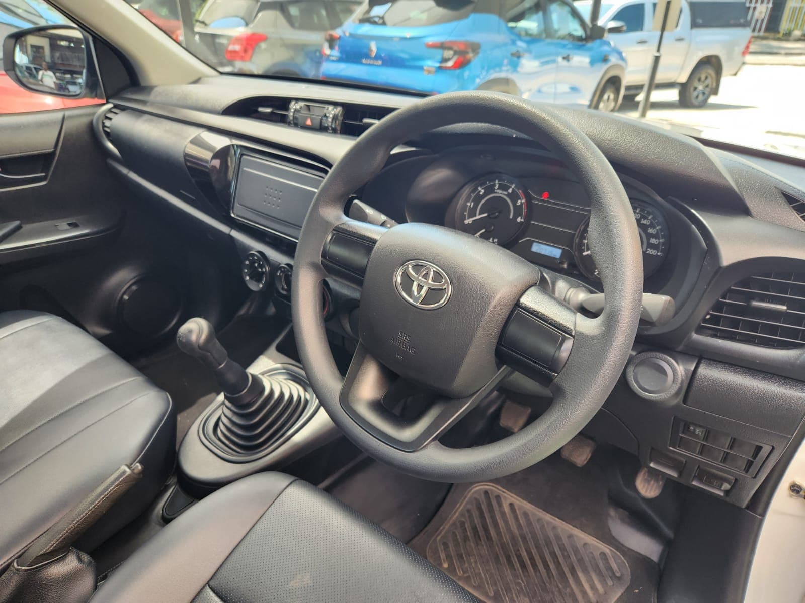 Interior cabin view of the 2025 Toyota Hilux 2.4 GD Single-Cab, showing dashboard, steering wheel and manual gear lever.