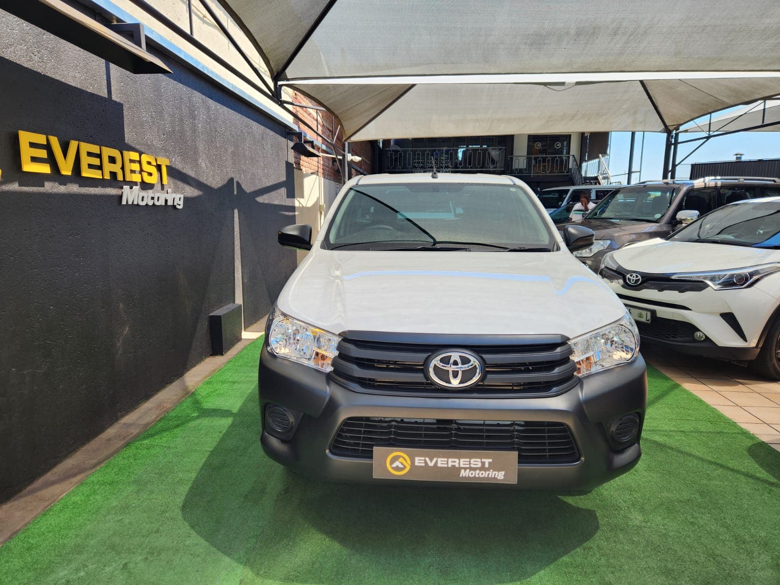 Front exterior view of the white 2025 Toyota Hilux 2.4 GD Single-Cab, parked under dealership canopy.